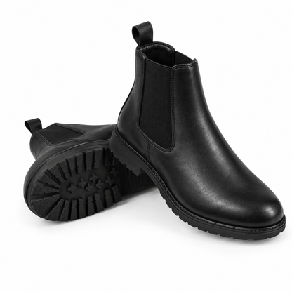 A pair of black leather Chelsea boots, with one boot standing upright to show the side profile and elastic side gore, and the other lying on its side to display the textured black rubber sole.